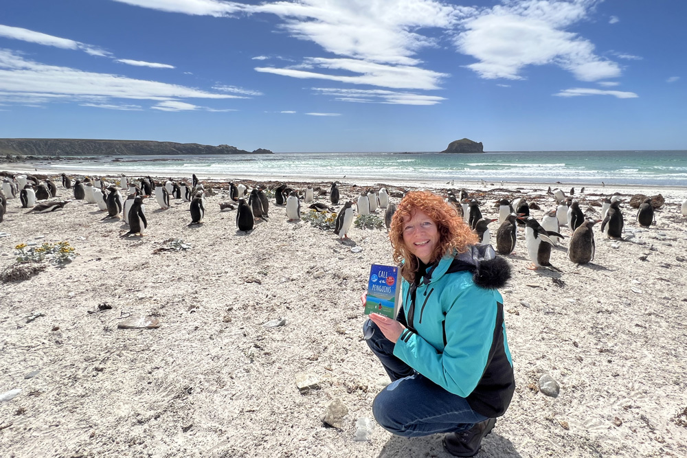Hazel Prior on a beach surrounded by penguins