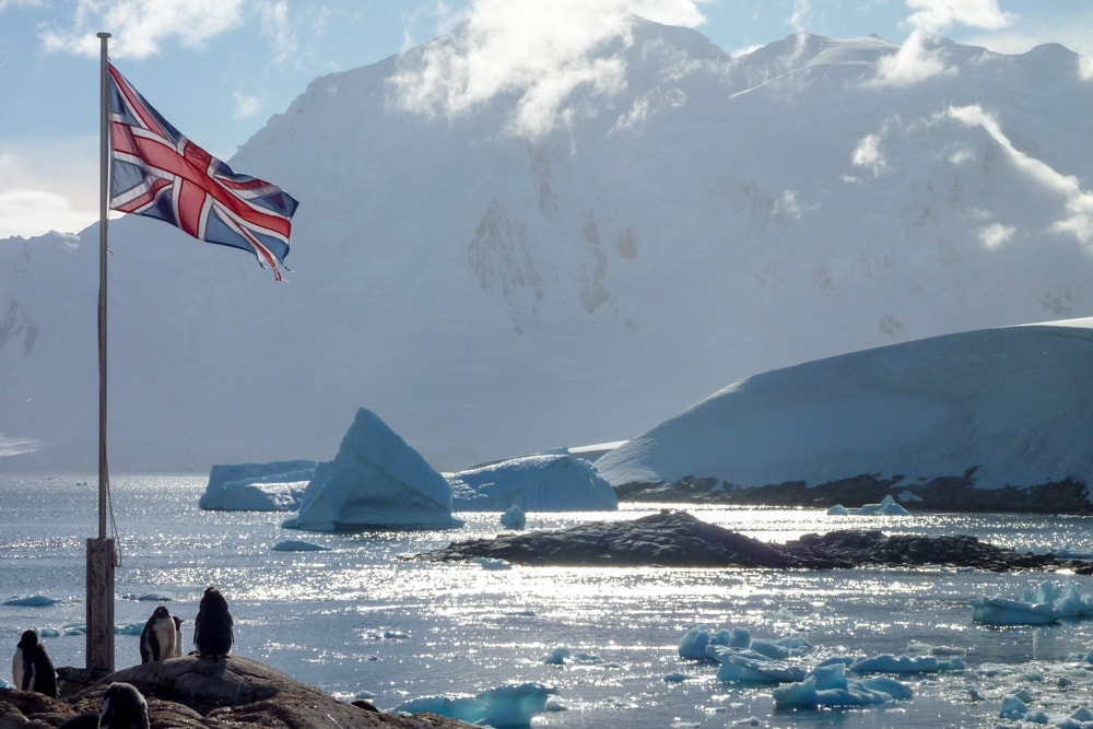 Icebergs in the bay with the UK flag and penguins in the foreground