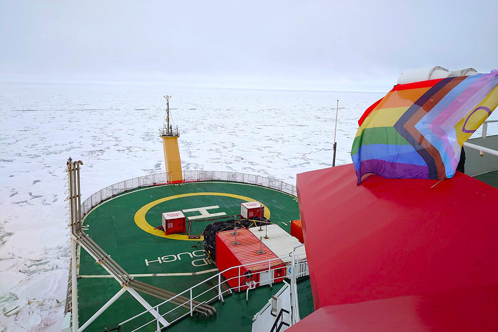 An icebreaker surrounded by ice flying the pride flag