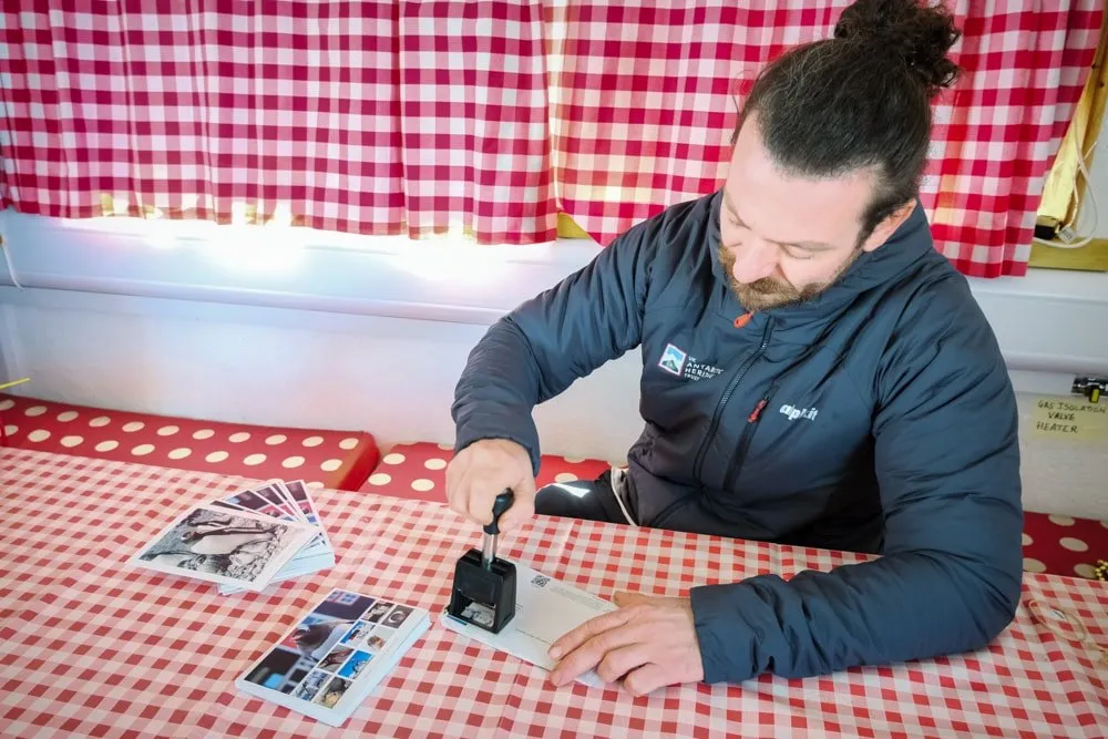 George sat at a red clothed table stampign postcards