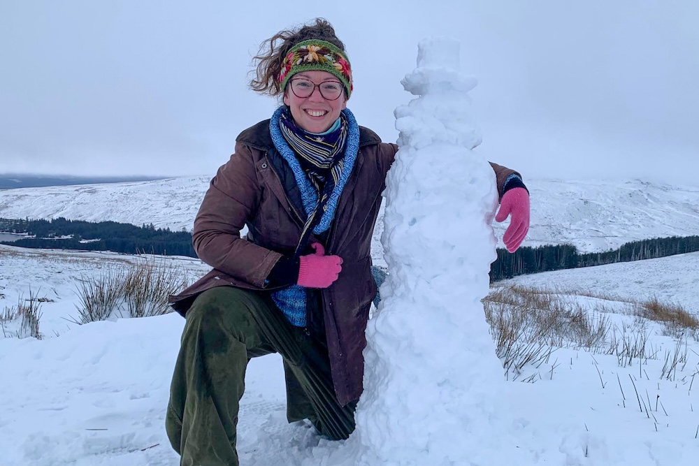 Conservation carpenter Kate Walford hugging a snowman in a snowy environment